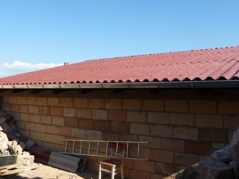 Neubaudach mit stabilen Faserzement Wellplatten Frisch verlegtes Dach aus roten Faserzement Wellplatten, Baustelle im Vordergrund